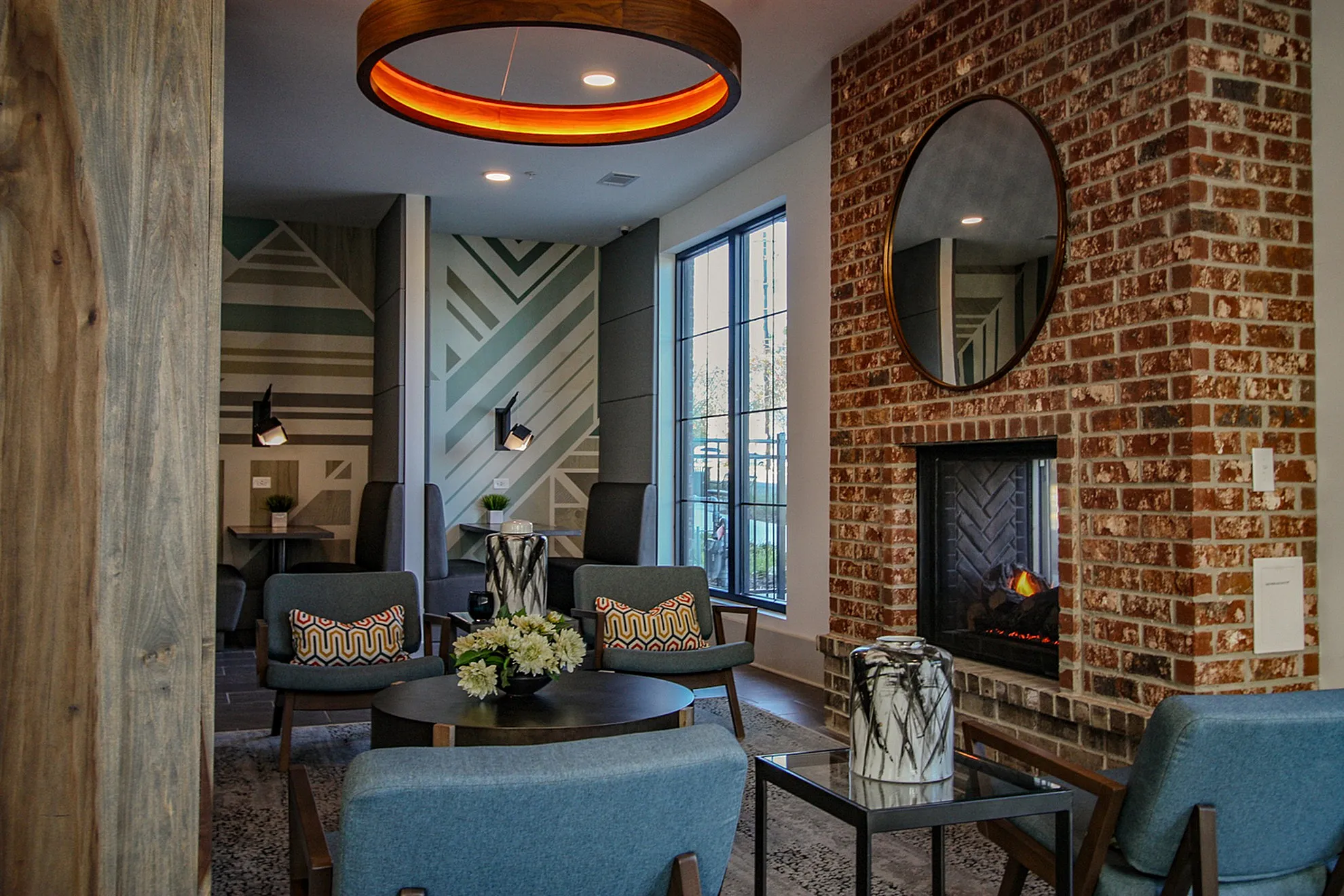 Chic modern apartment lounge featuring cozy blue seating, stylish geometric wall art, a warm brick fireplace, and elegant lighting.