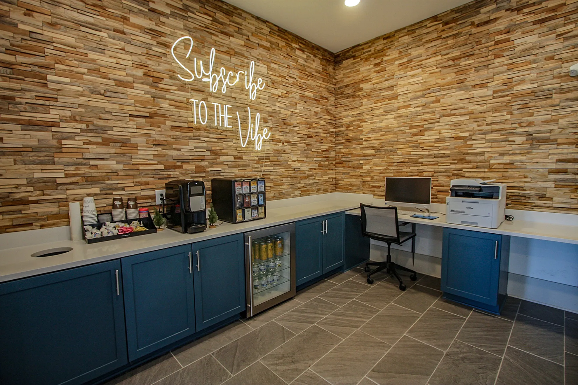Chic communal workspace with modern stone accent wall, coffee station, and sleek office amenities.