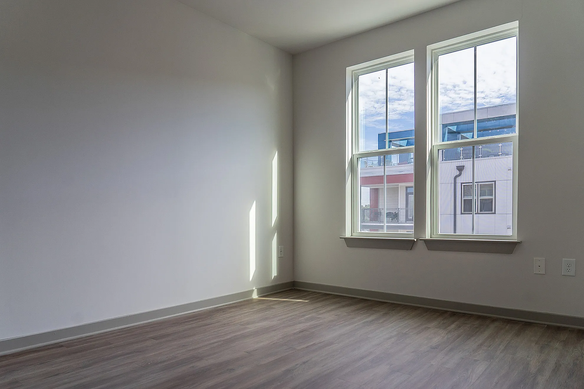 Bright, sunlit room with sleek wooden flooring and large windows offering a modern urban view.