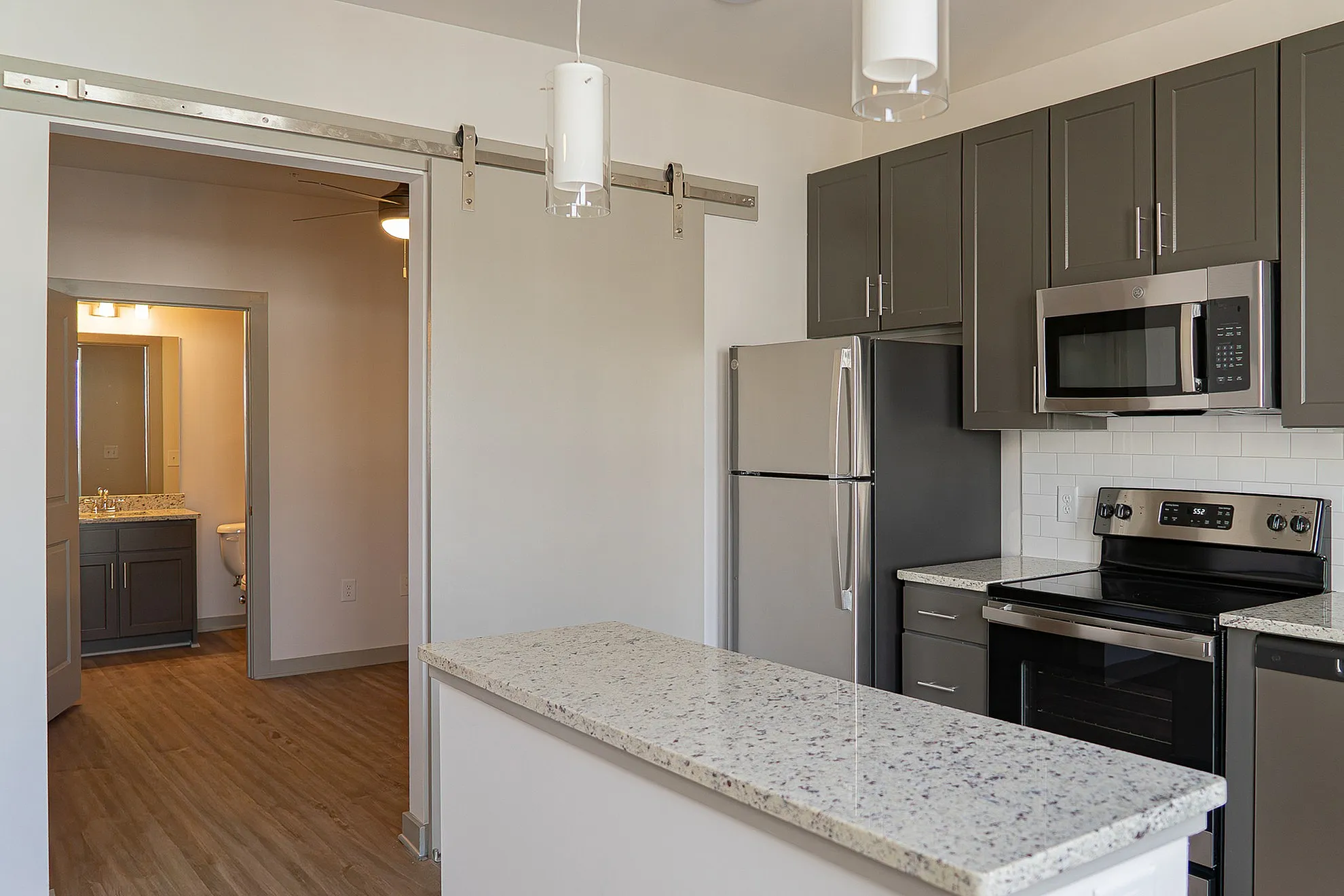 Modern kitchen with sleek grey cabinets, stainless steel appliances, and a stylish granite countertop, leading into a cozy bathroom.