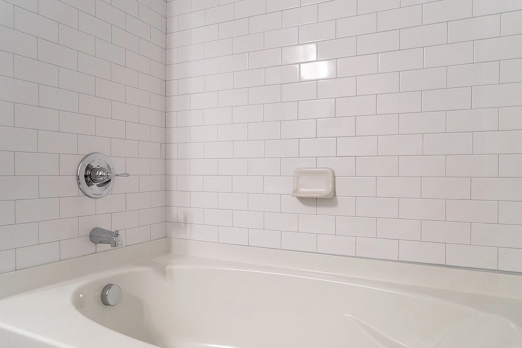 Elegant bathroom showcasing a pristine white-tiled wall and a modern bathtub, highlighting luxury and comfort.