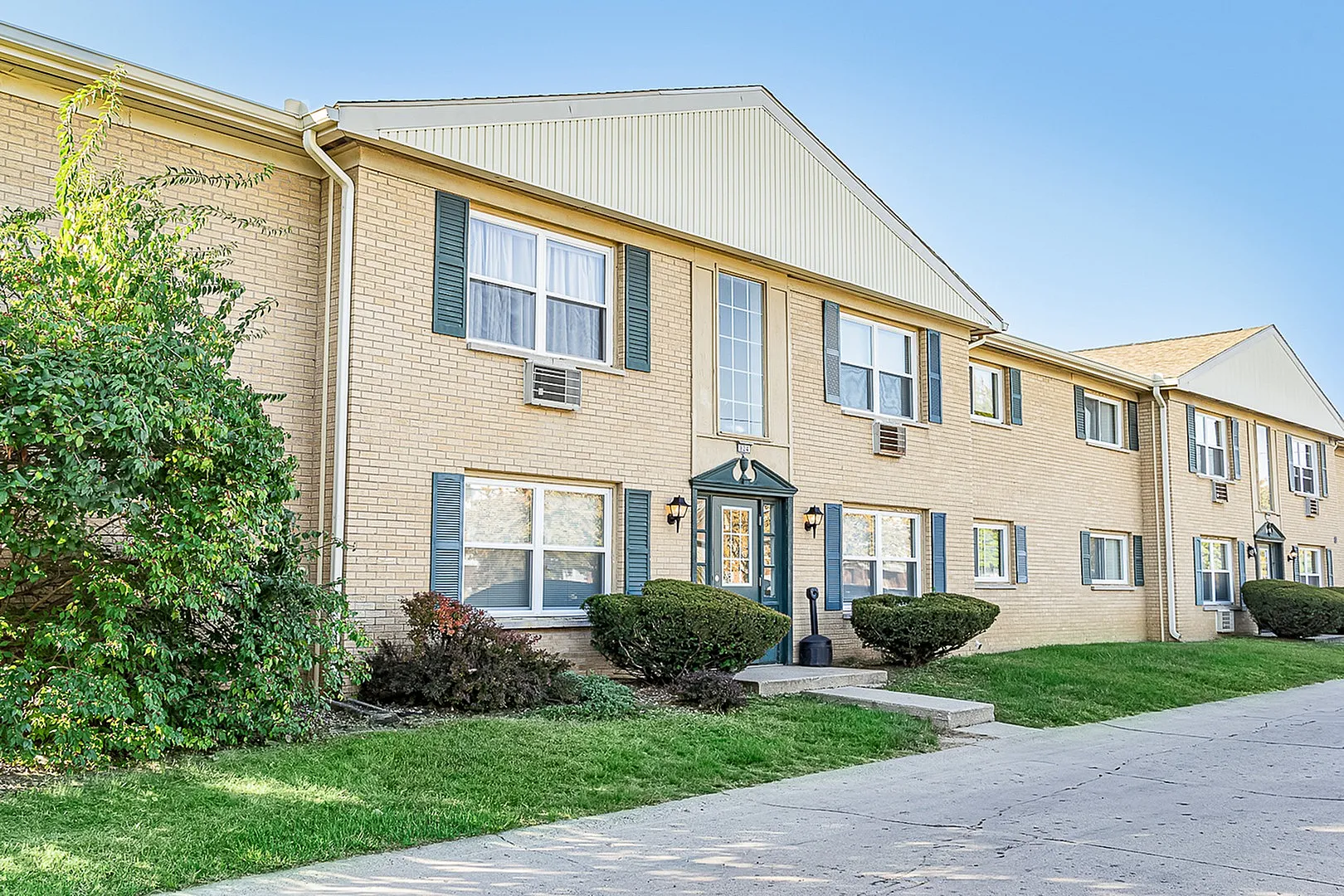 Charming two-story apartment building with classic brick facade, lush green landscaping, and inviting front entrance.