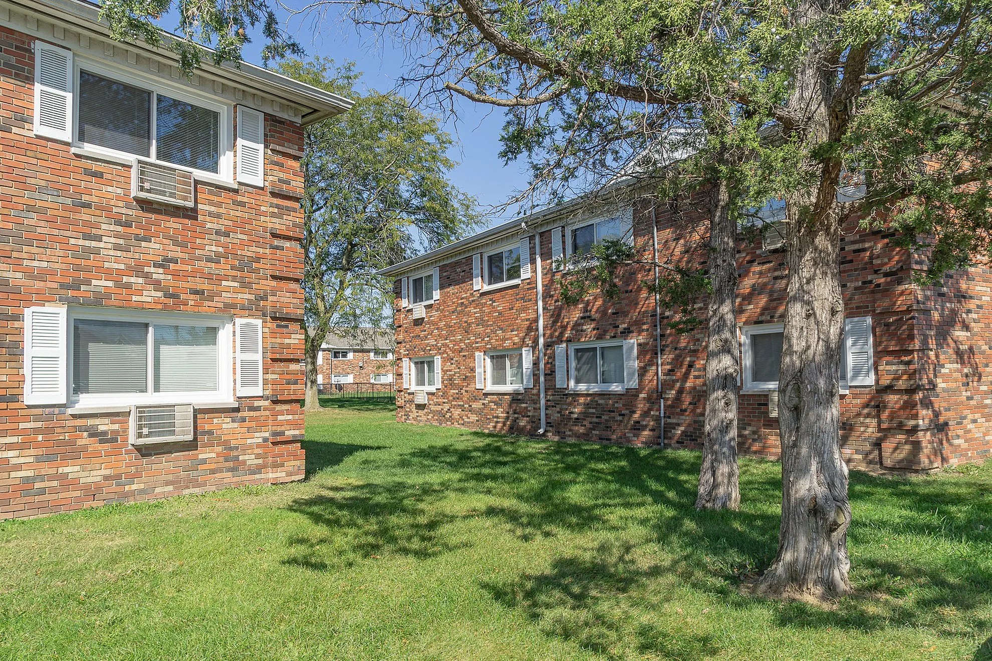 Charming brick apartment buildings surrounded by lush greenery and mature trees, offering a serene residential environment.