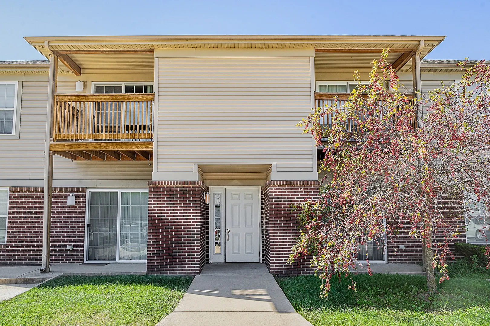 Charming two-story apartment exterior featuring a private balcony, manicured lawn, and vibrant landscaping for a welcoming atmosphere.