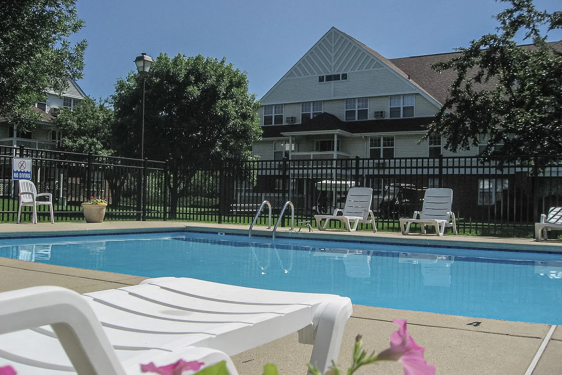 Charming apartment building with a refreshing outdoor pool and relaxing lounge chairs, surrounded by lush greenery.