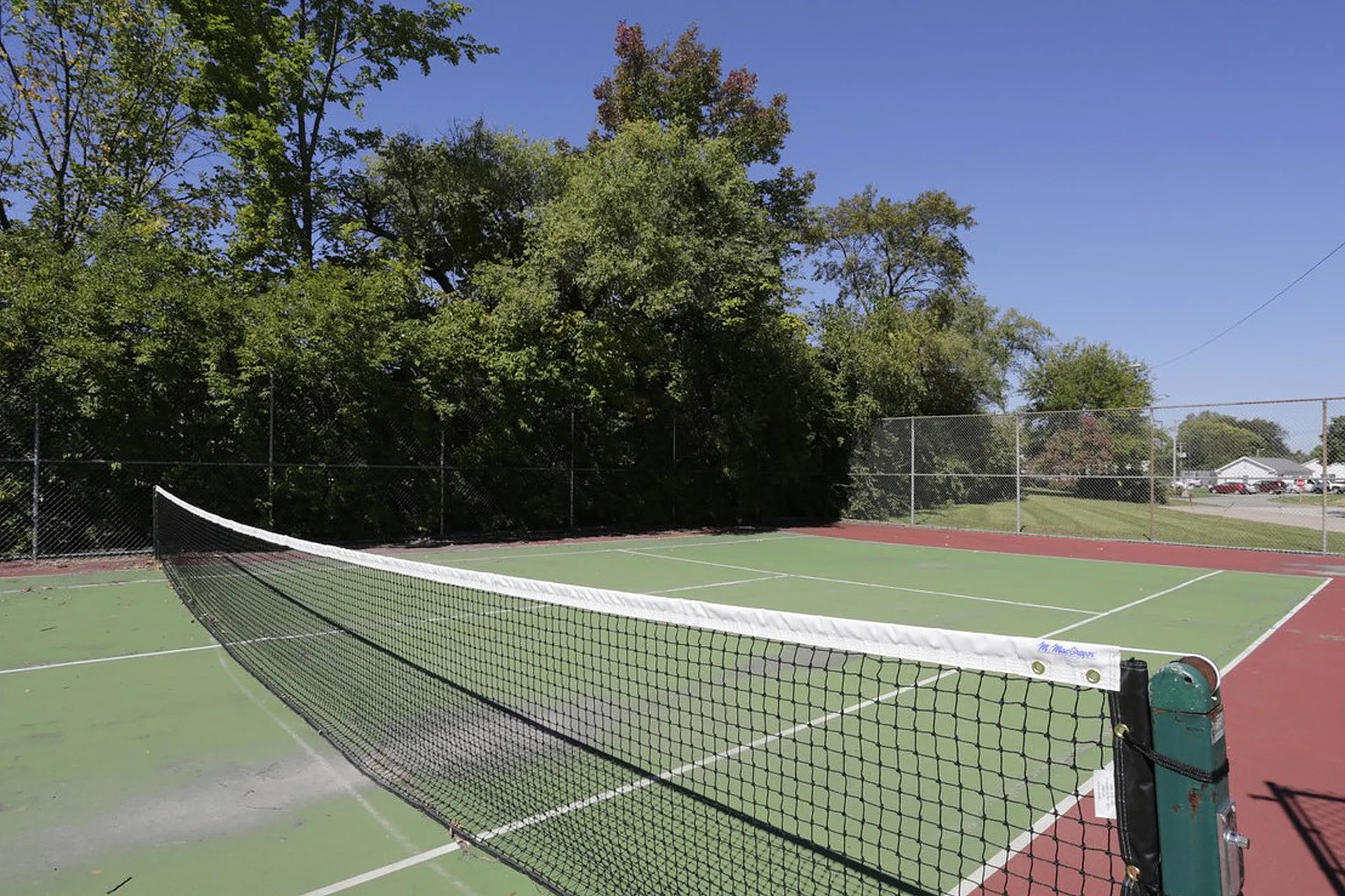 Inviting outdoor tennis court surrounded by lush greenery, perfect for recreational play on a sunny day.