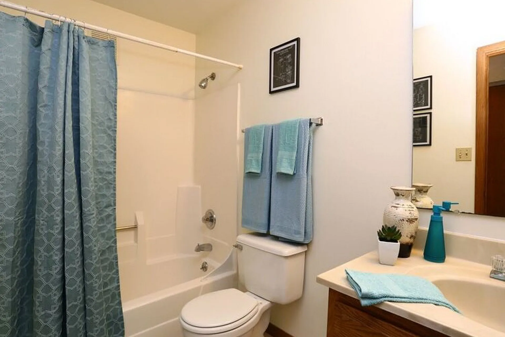 Elegant bathroom with a soothing blue theme, featuring a modern shower-tub combo, stylish vanity with decorative vases, and plush towels for a luxurious touch.