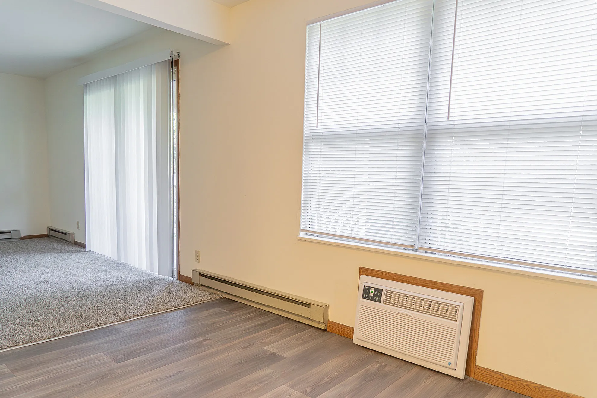 Bright living room featuring elegant flooring, expansive windows with blinds, and a cozy carpeted area leading to a patio through stylish sliding doors.