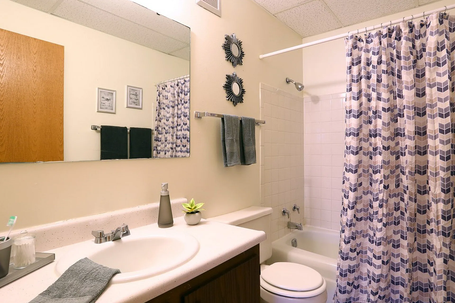 Bright and inviting bathroom featuring a modern vanity, stylish mirror decor, and fresh accents with a geometric shower curtain.
