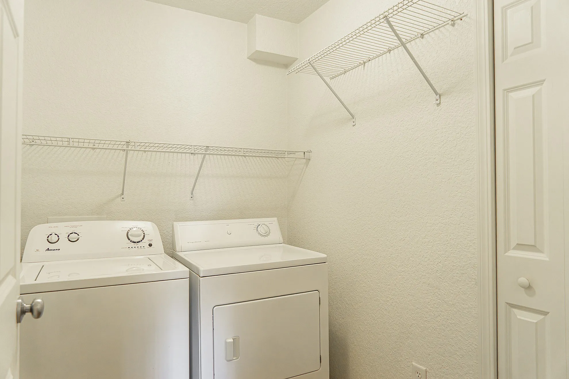 Modern laundry room equipped with Amana washer and Frigidaire dryer, accentuated by convenient wire shelving.