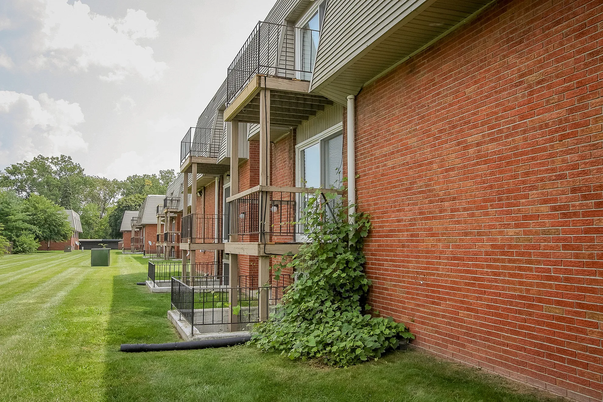 Charming brick apartment building with private balconies overlooking lush green lawns, perfect for serene living.