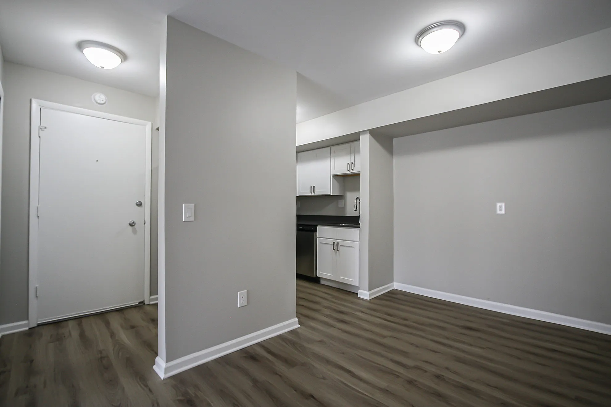Modern apartment with stylish open entryway, featuring sleek wood flooring and a cozy kitchen with crisp white cabinetry.