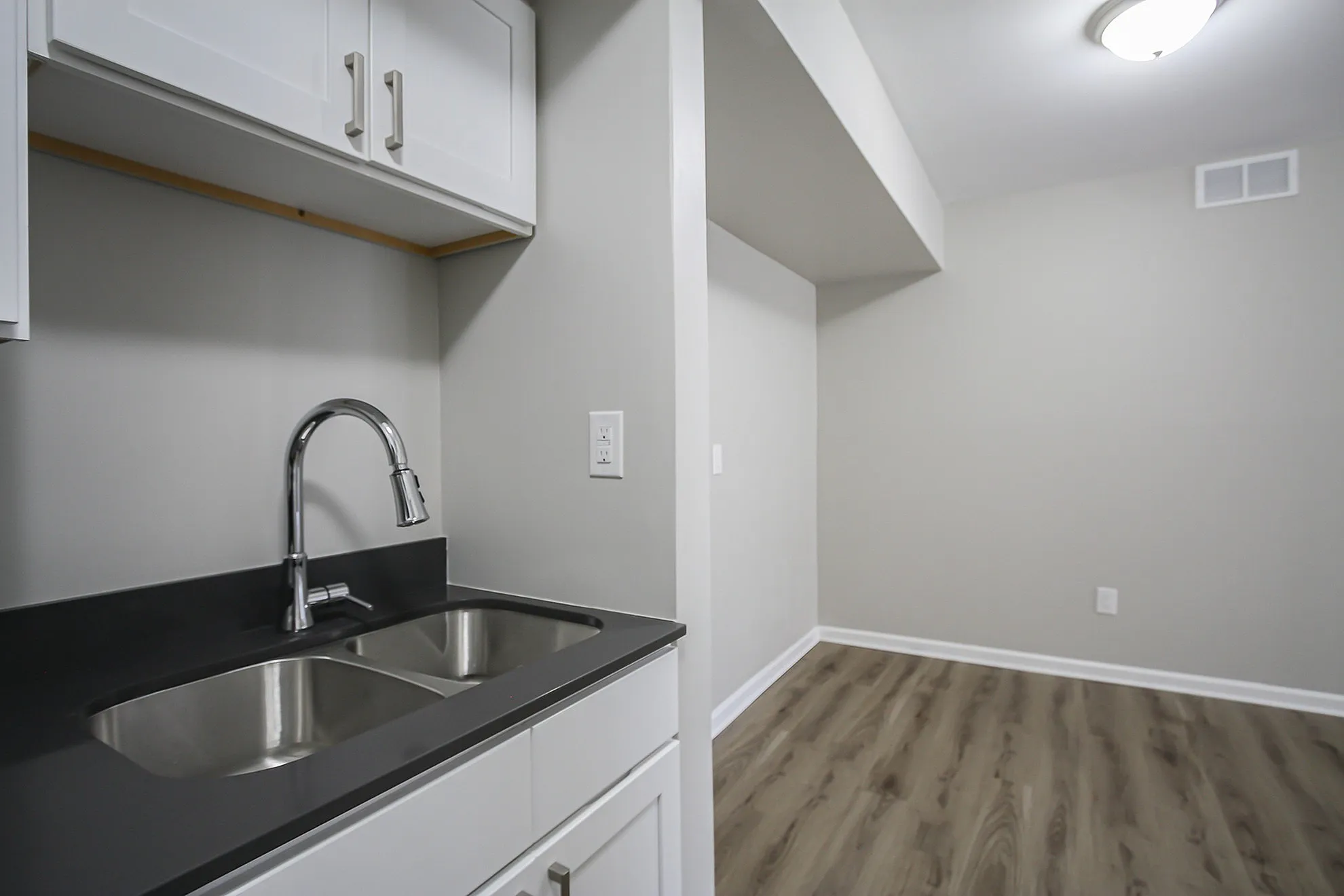 Chic kitchen nook with sleek modern double sink, elegant white cabinetry, and warm wood floors in a cozy apartment setting.