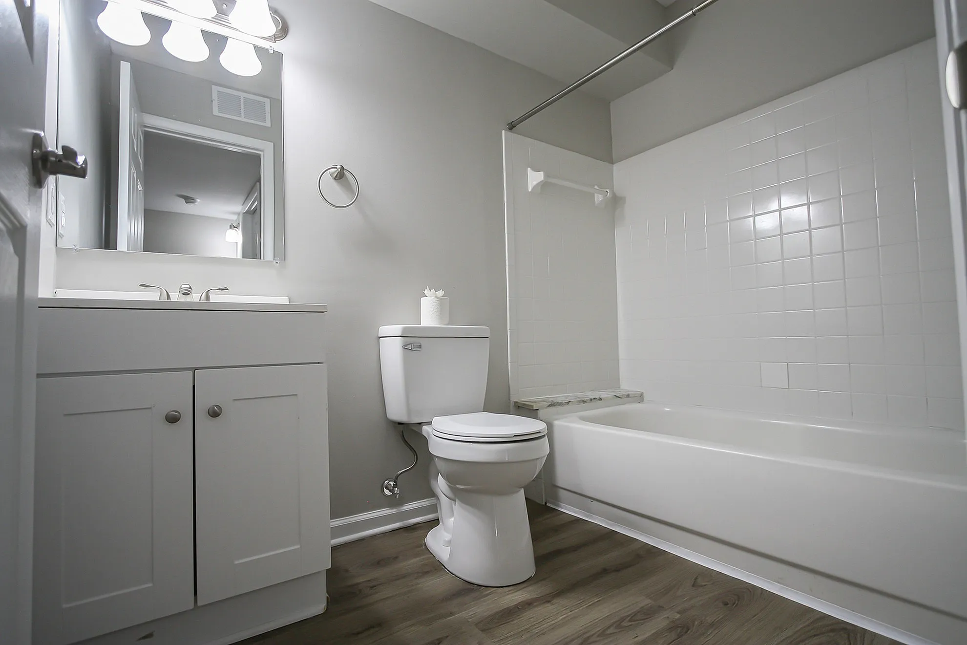 Modern bathroom featuring sleek white fixtures, a spacious bathtub, and stylish wood flooring.