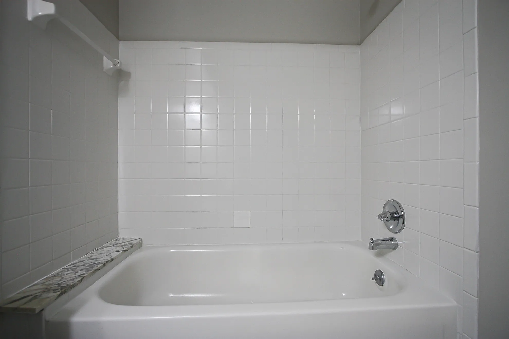 Elegant bathroom featuring a pristine white bathtub with modern chrome fixtures, complemented by stylish white tiled walls.