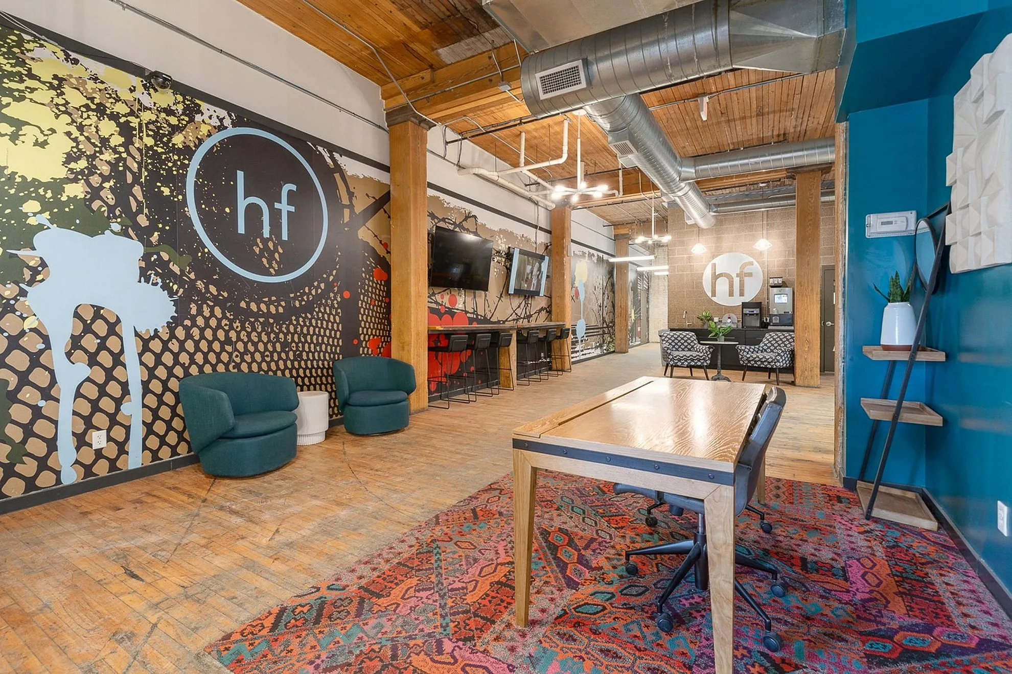 Contemporary office space with vibrant wall art, cozy seating, and wooden accents featuring an industrial design.
