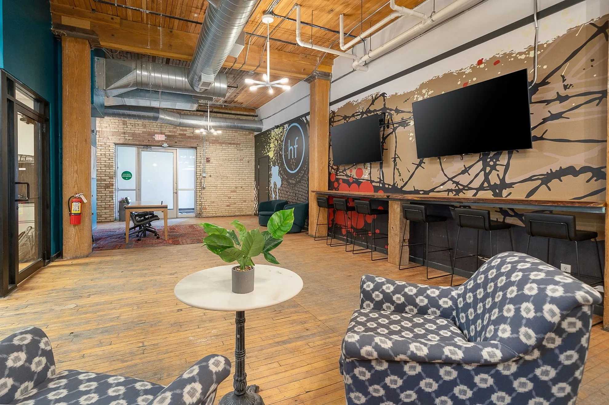 Trendy loft-style lounge with industrial design, featuring cozy seating, vibrant artwork, and rustic wooden floors.