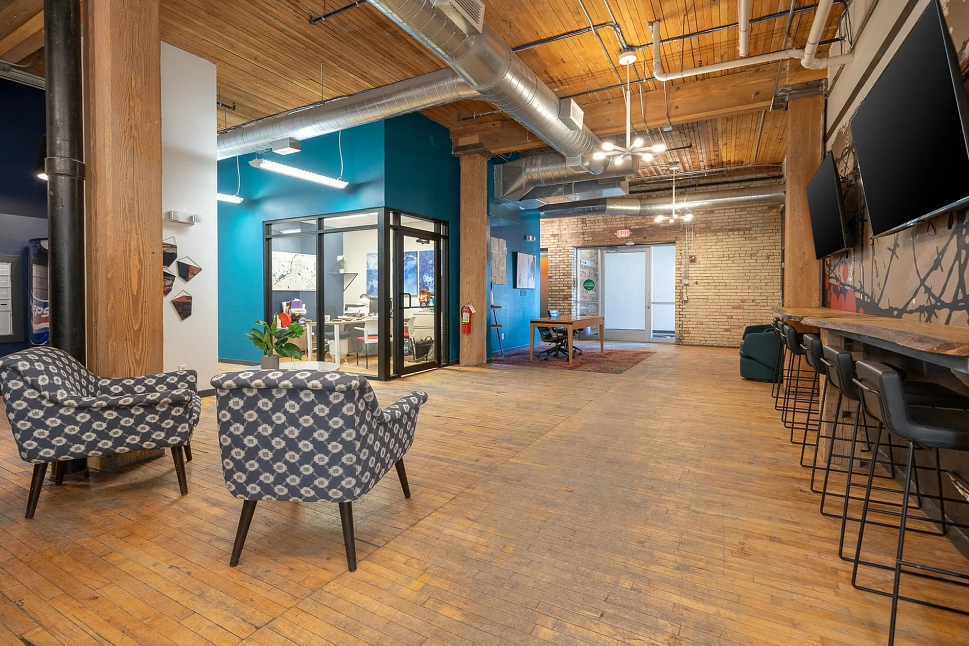 Chic industrial-style office space with exposed brick and wood beams, featuring modern seating and vibrant artwork.