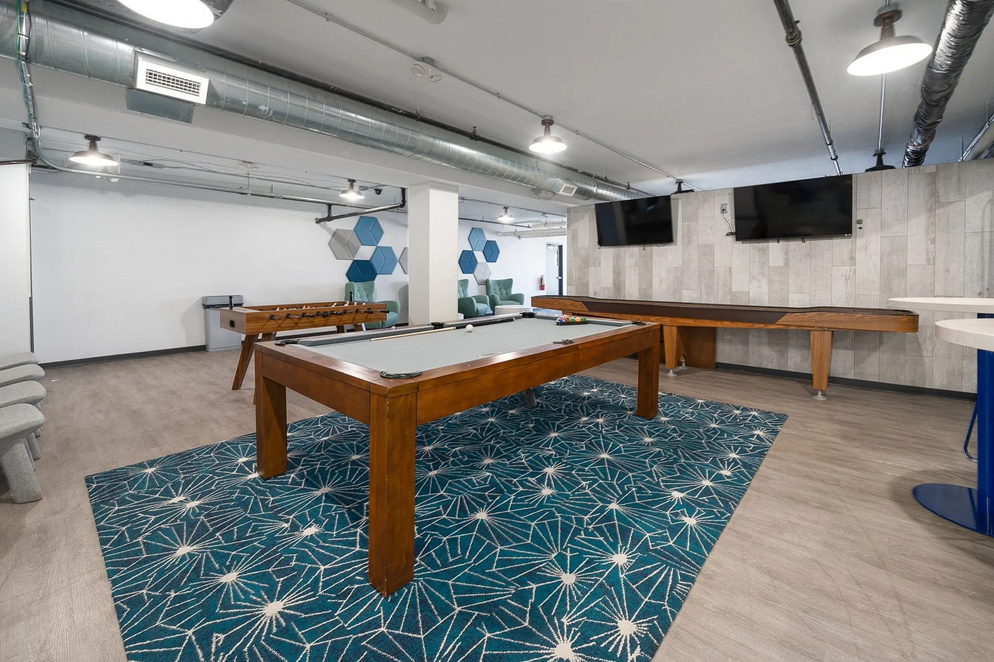 Chic recreational room boasting a pool table, foosball, and shuffleboard on a stylish blue-patterned rug, perfect for entertainment.