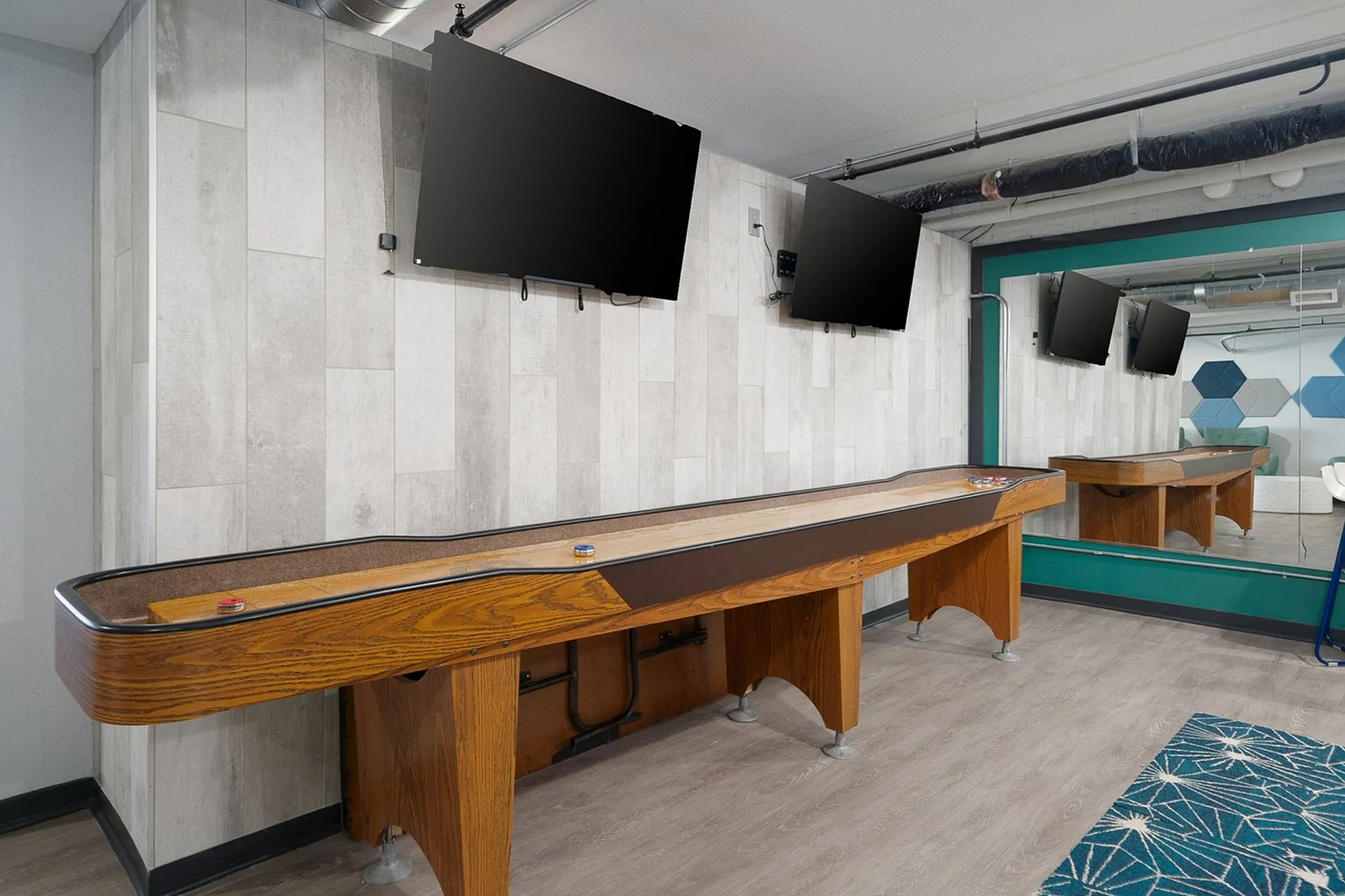 Modern entertainment room featuring a sleek shuffleboard table, dual mounted TVs, and contemporary decor.