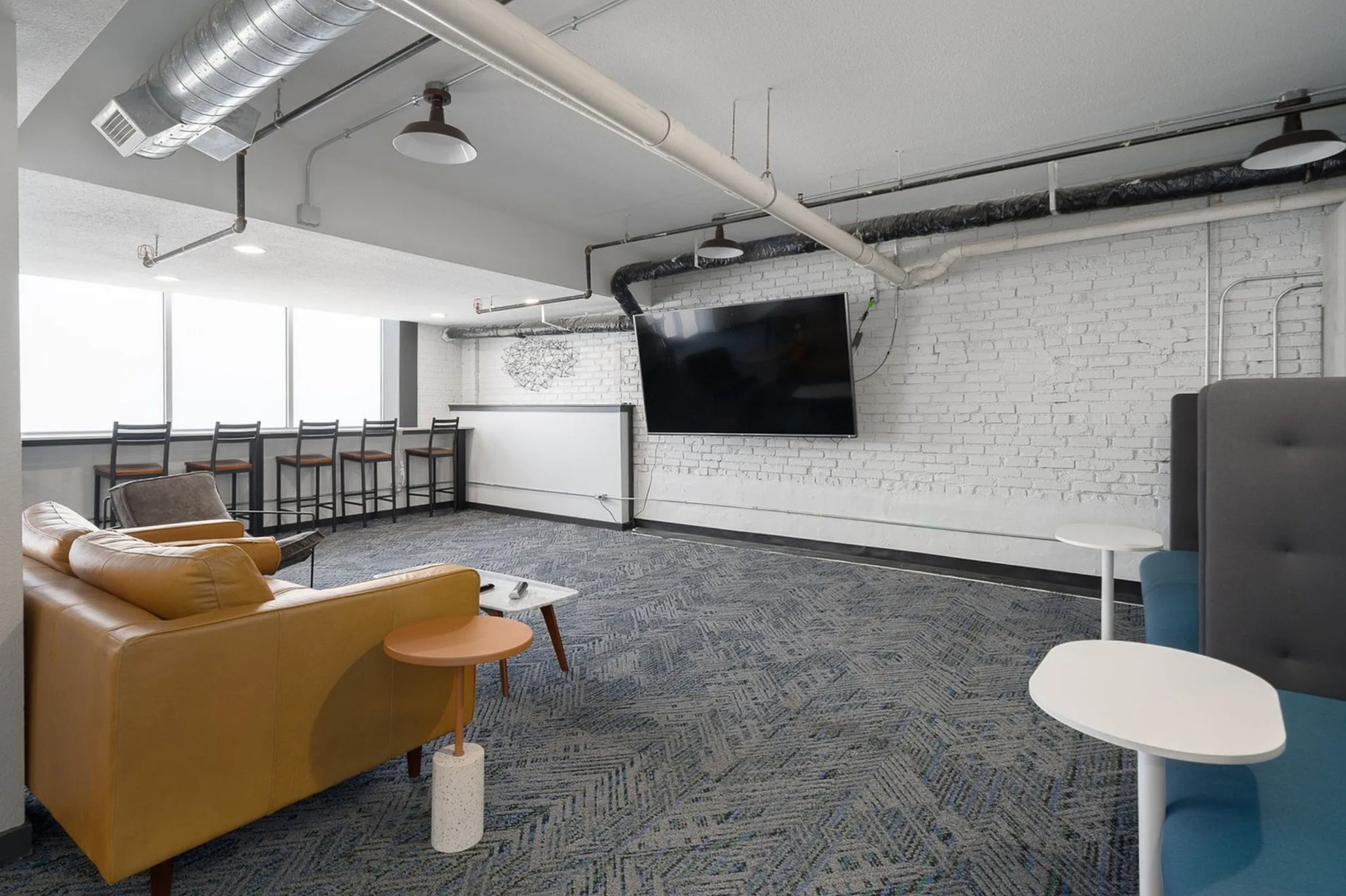 Chic modern apartment lounge with industrial-style piping, plush seating, and a large flat-screen TV on a white brick wall.