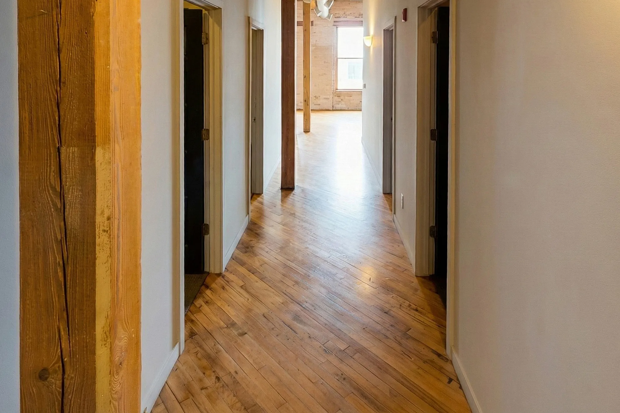Inviting hallway featuring warm wooden floors, leading to spacious, well-lit rooms.