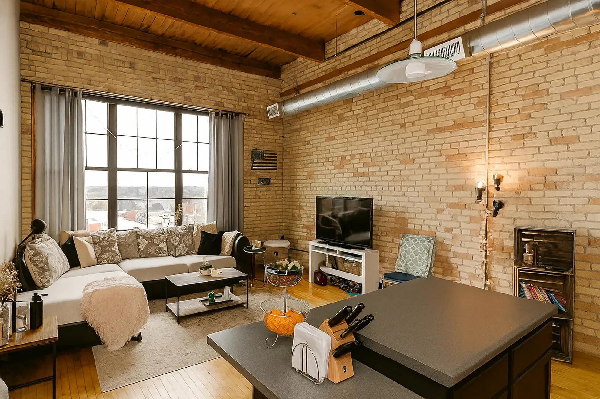 Chic urban living room with exposed brick walls, large windows, and modern decor, perfect for a cozy city lifestyle.