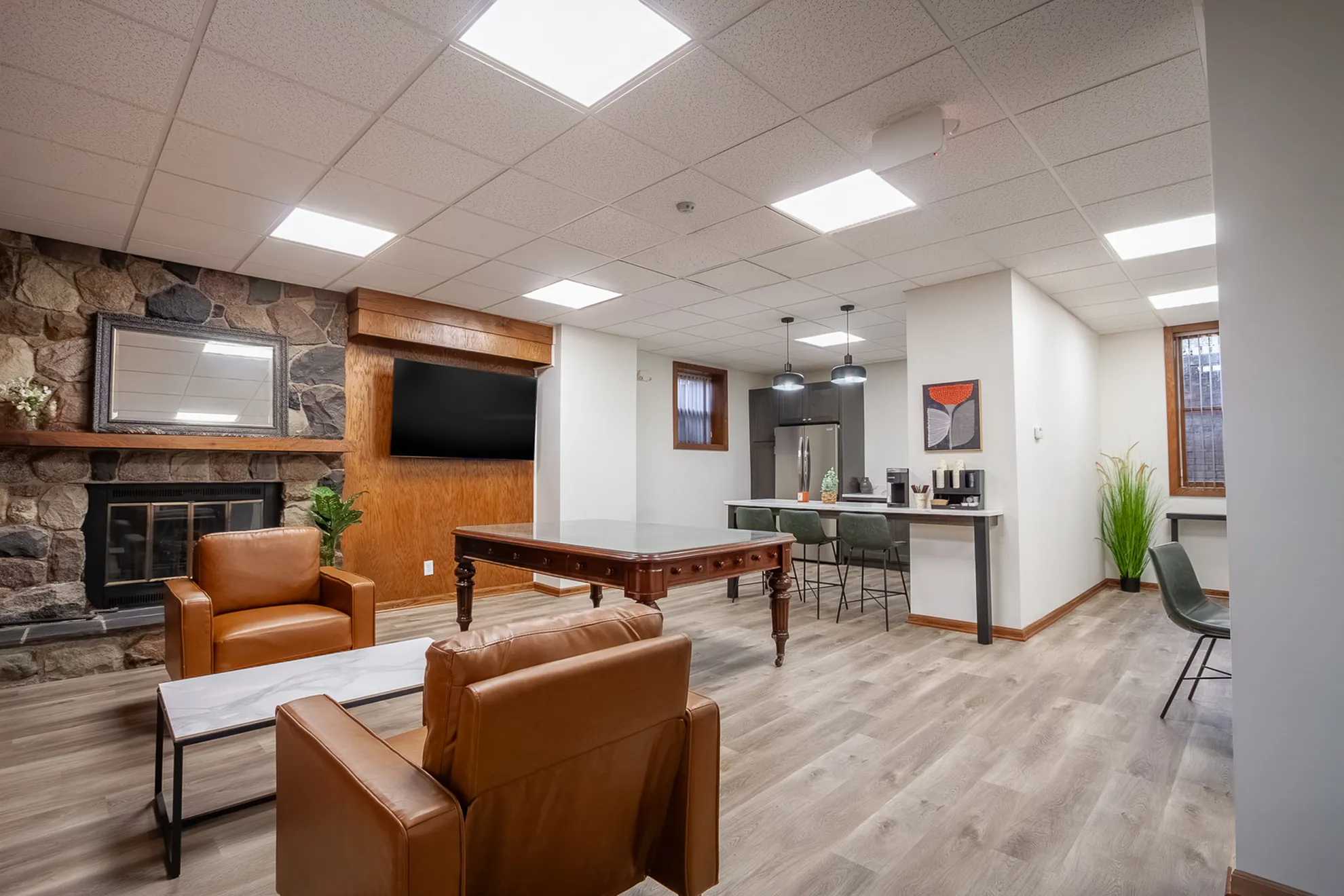 Elegant living area with a stone fireplace, plush leather seating, chic kitchen bar, and ambient lighting, perfect for luxurious gatherings.