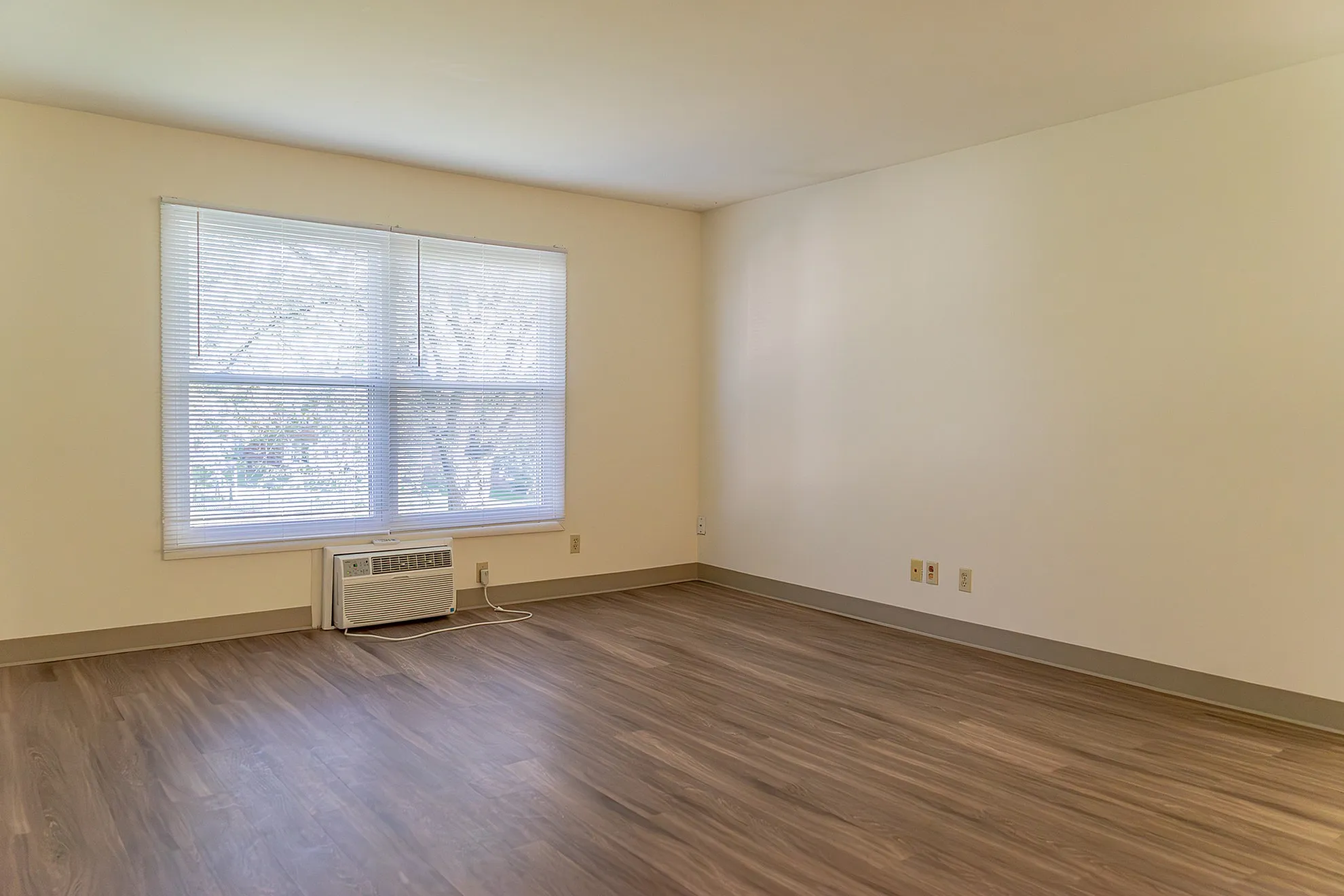 Bright and inviting empty room with large windows, neutral walls, and elegant wooden flooring, perfect for a stylish living space.