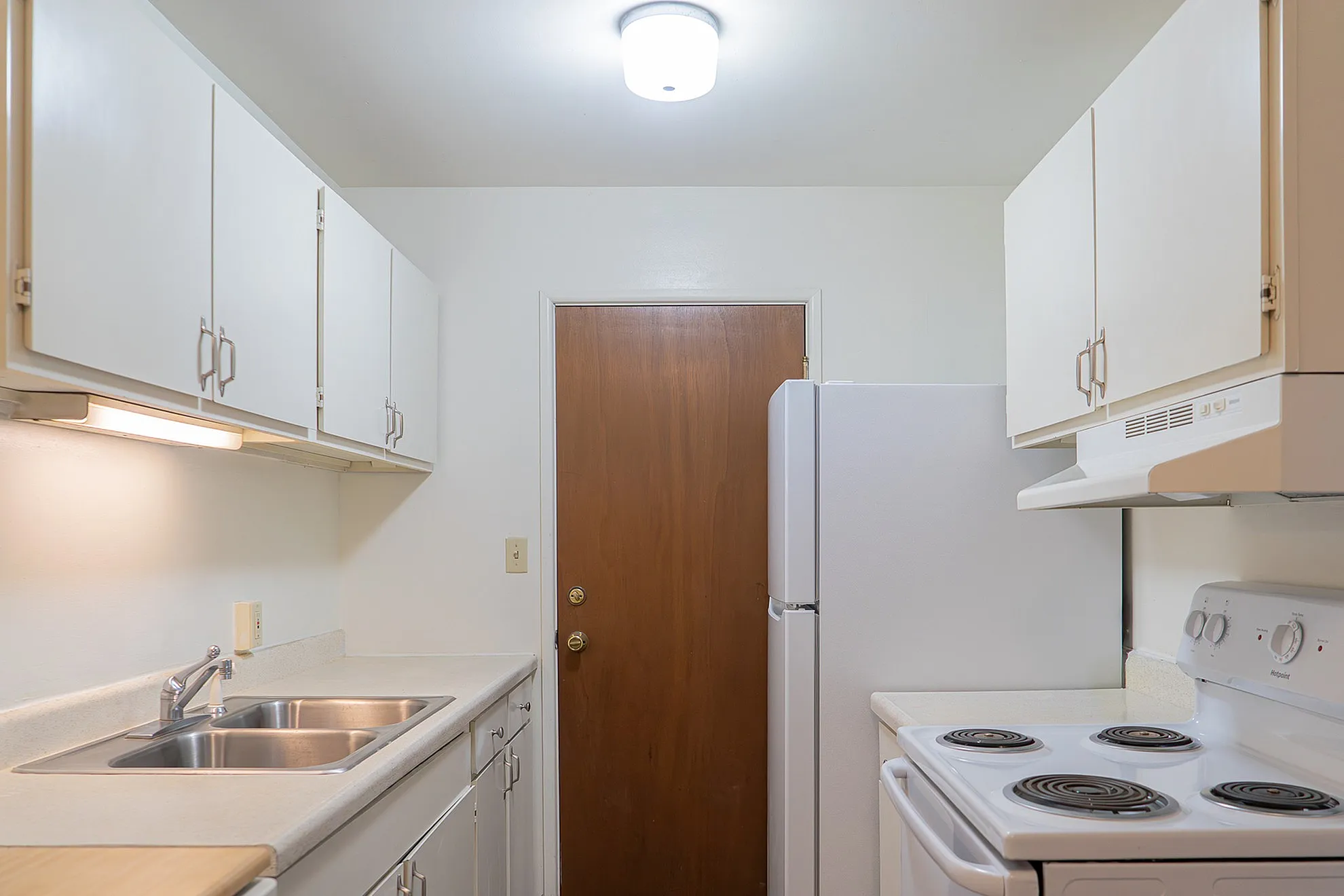 Bright and clean kitchen featuring white cabinetry, modern appliances, and a spacious countertop with dual sinks.