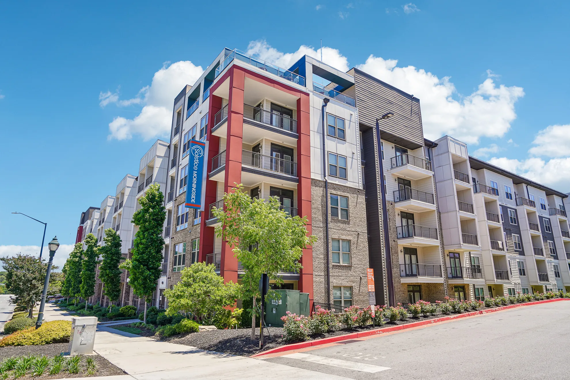 Modern apartment complex with a sleek design, featuring spacious balconies against a backdrop of clear blue skies and vibrant landscaping.