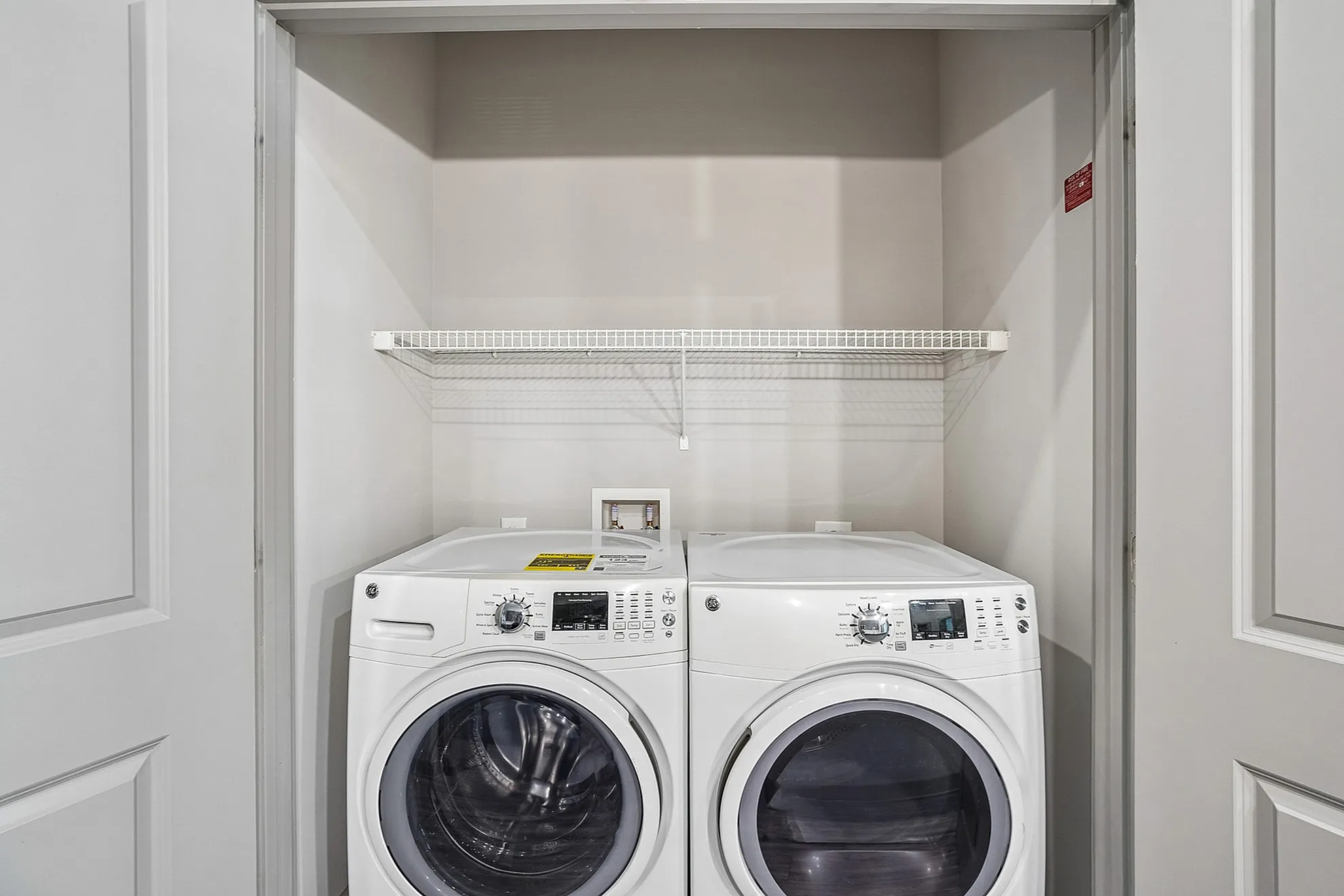 Modern laundry area featuring sleek front-loading washer and dryer with convenient overhead shelving in a compact space.