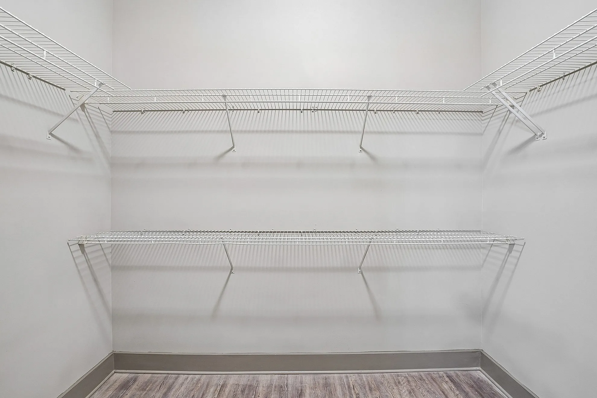 Spacious walk-in closet with sleek white shelving and elegant wood flooring, perfect for organized living.