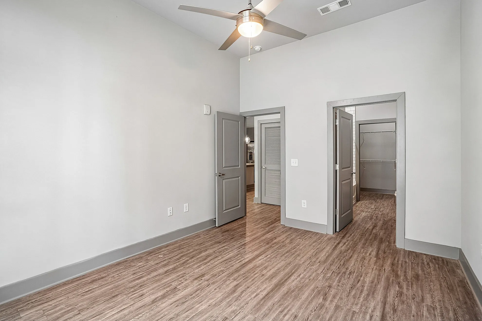 Bright, modern room with sleek wooden flooring, ceiling fan, and ample closet space, perfect for a stylish apartment.