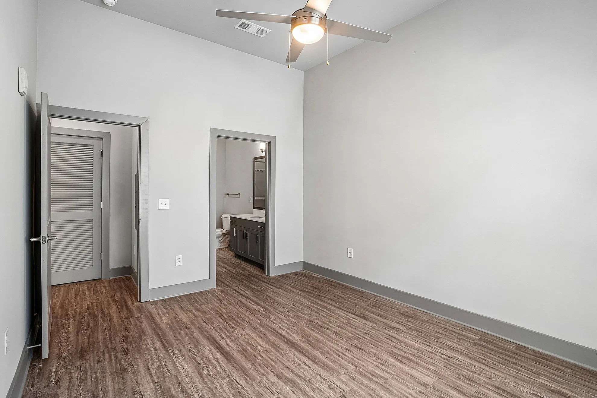 Modern bedroom with sleek wooden flooring, ceiling fan, and an en-suite bathroom for optimal comfort and style.
