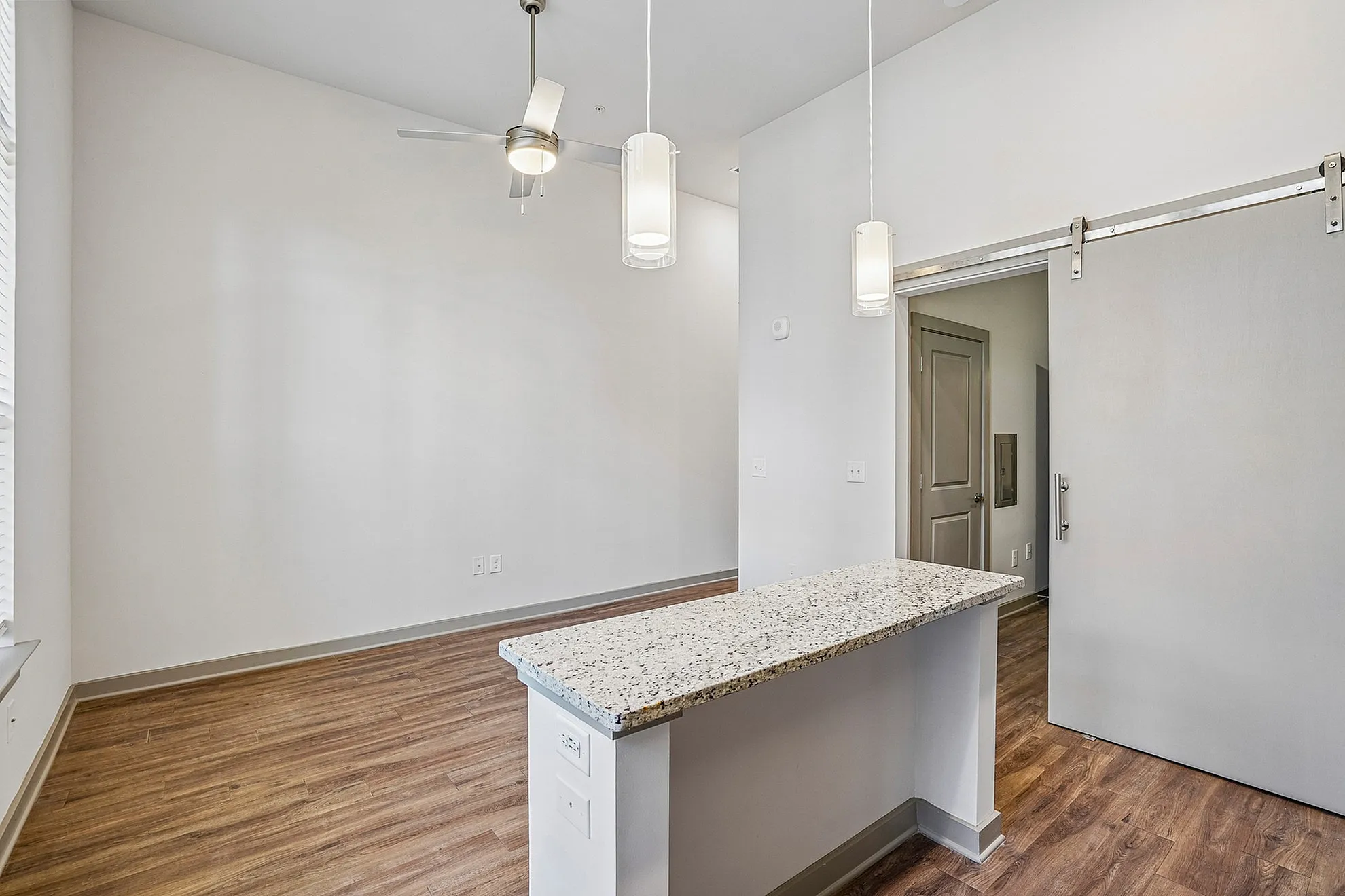 Modern apartment interior showcasing sleek hardwood floors, a stylish granite countertop, pendant lighting, and an open living space with a sliding door.
