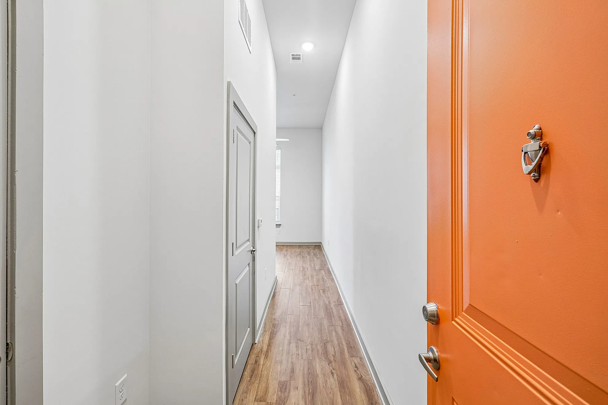 Inviting hallway with modern wood flooring and vibrant orange front door, leading into a well-lit space.