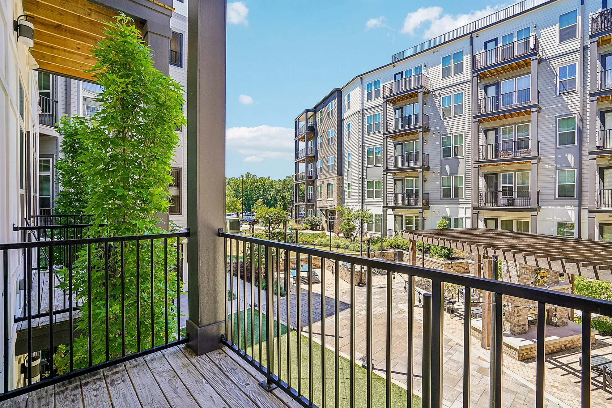 Charming apartment balcony overlooking a vibrant courtyard with modern multi-story buildings and lush landscape.