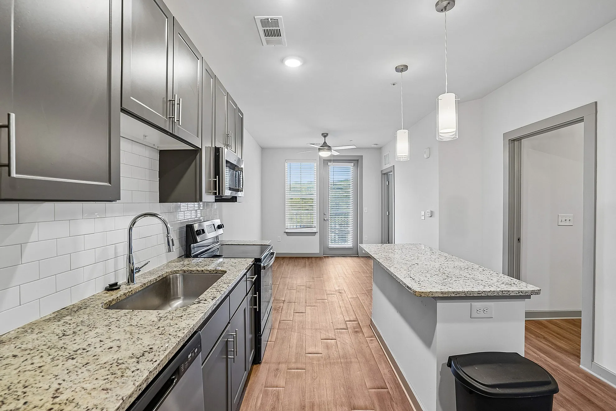 Modern kitchen with sleek gray cabinets, granite countertops, and open layout leading to a bright, inviting living area.