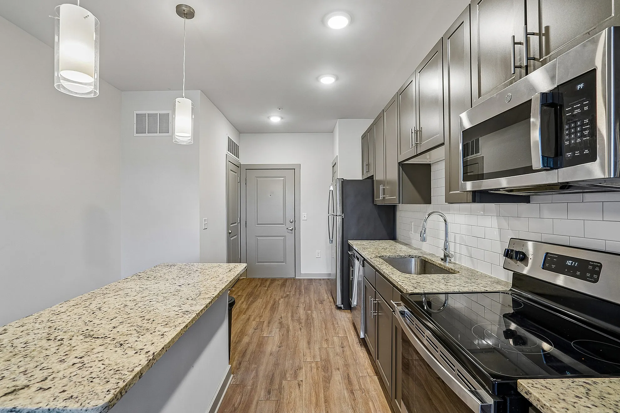 Contemporary kitchen with elegant granite countertops, stainless steel appliances, and sleek grey cabinetry, featuring ample lighting and a streamlined design.