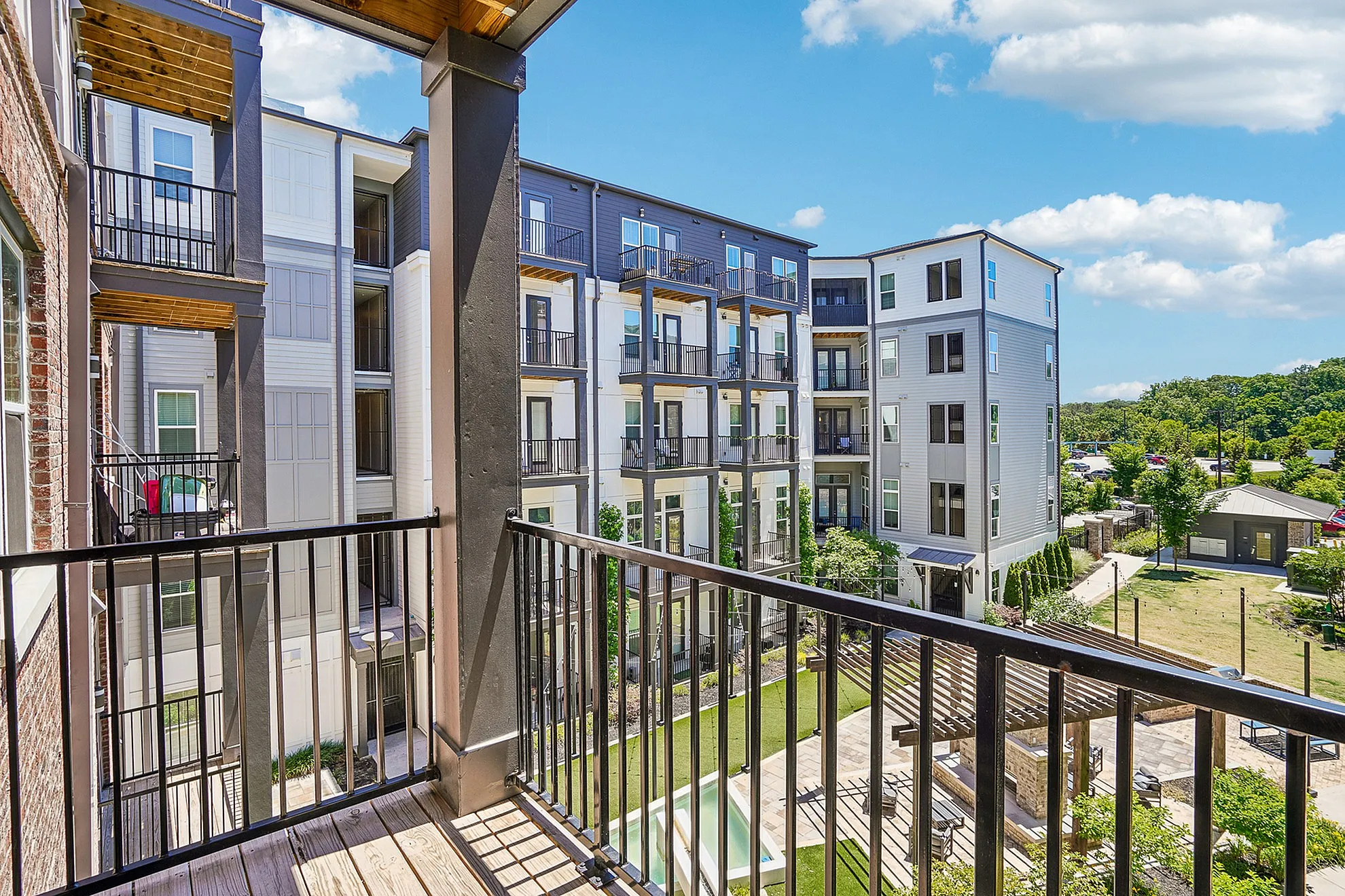 Contemporary apartment balcony view showcasing stylish multi-story buildings with lush landscaped courtyard and bright blue skies.