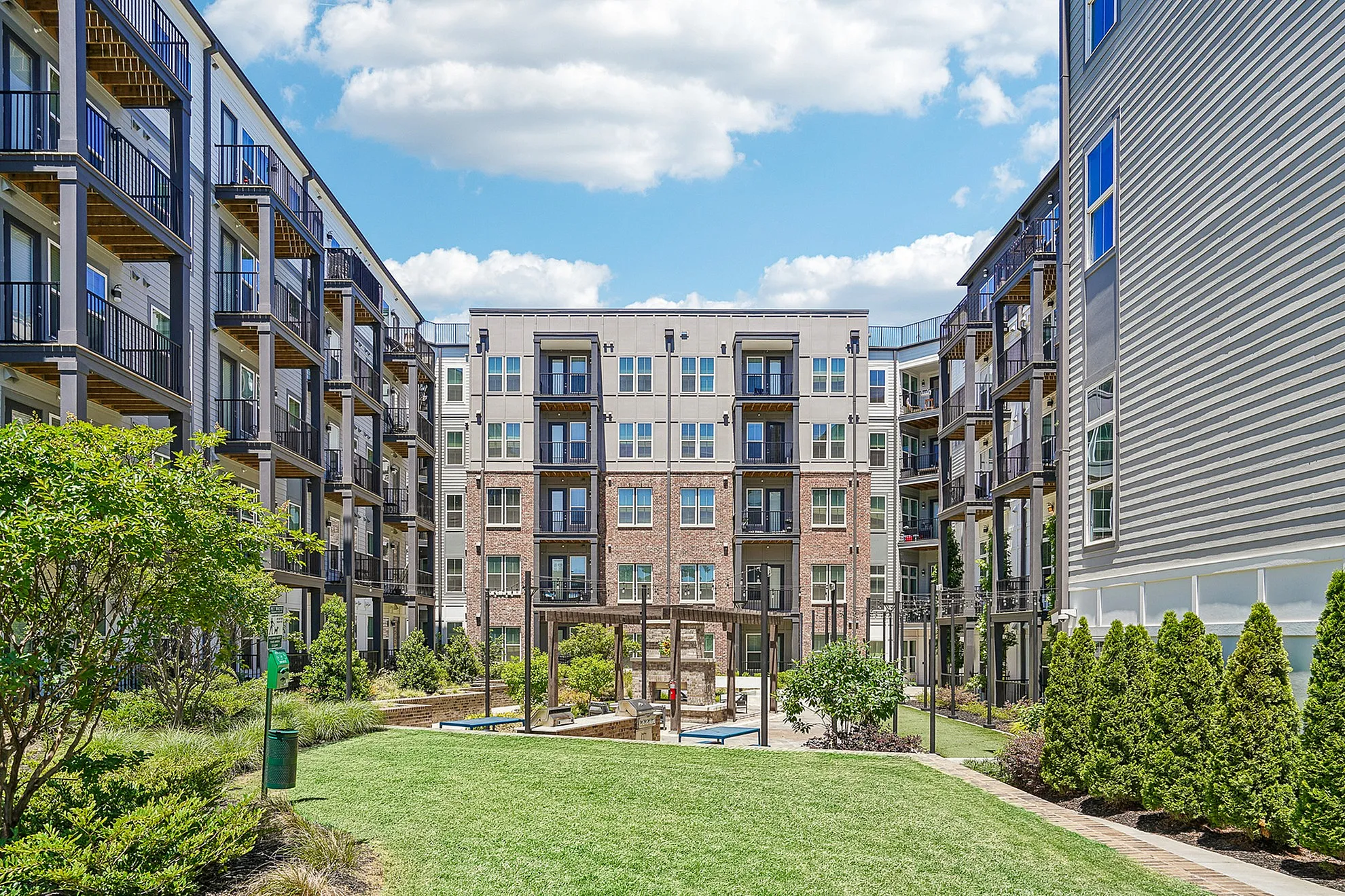 Modern apartment complex with landscaped green space, inviting balconies, and a vibrant urban vibe under a clear blue sky.