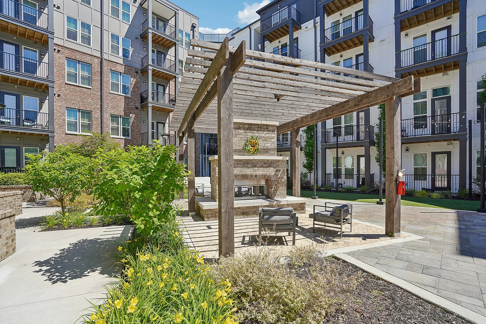 Charming outdoor courtyard with a rustic pergola and stylish seating, framed by modern apartments and lush landscaping.