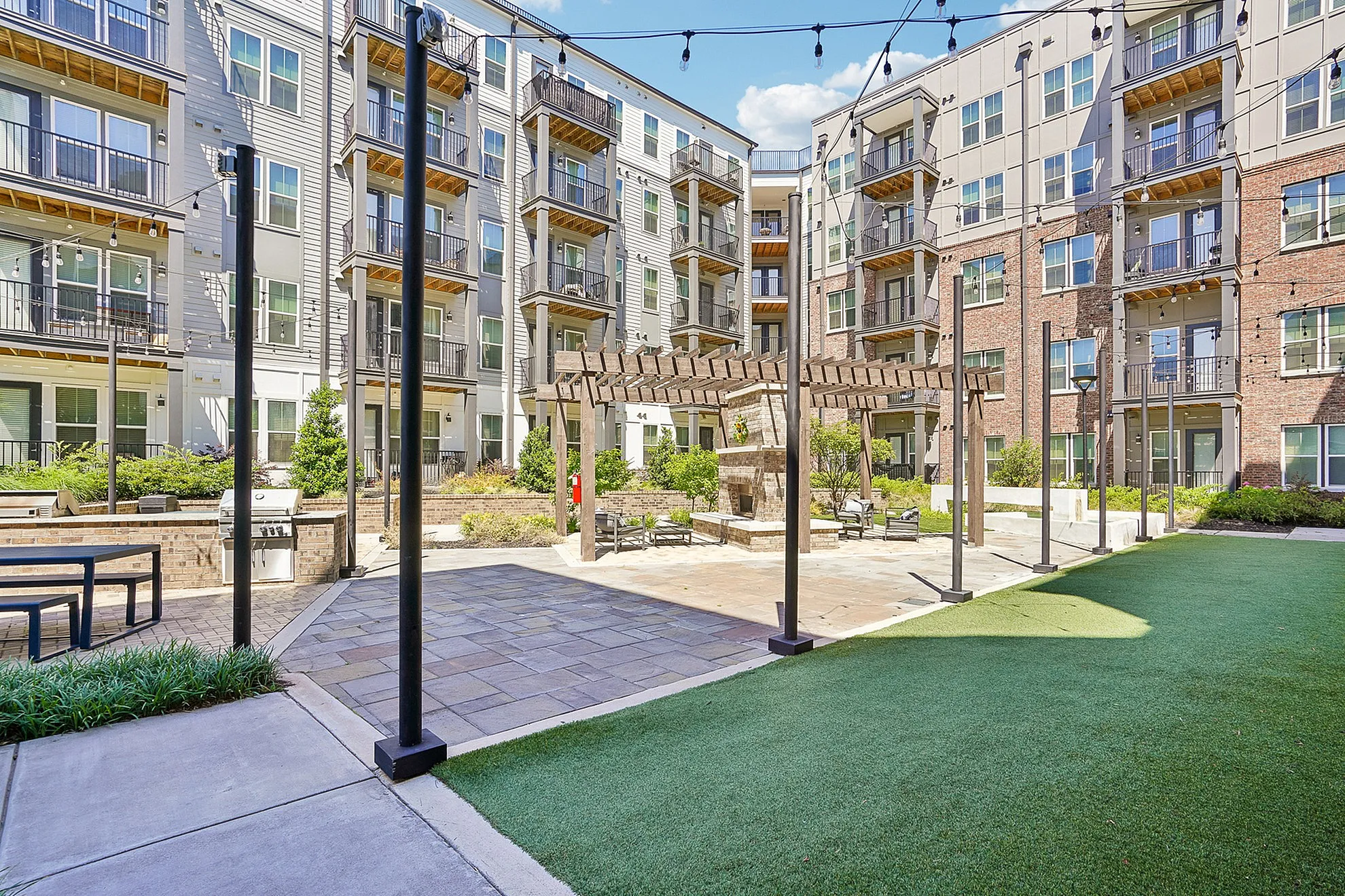 Contemporary apartment complex courtyard featuring vibrant greenery, stylish pergola, and inviting seating areas.