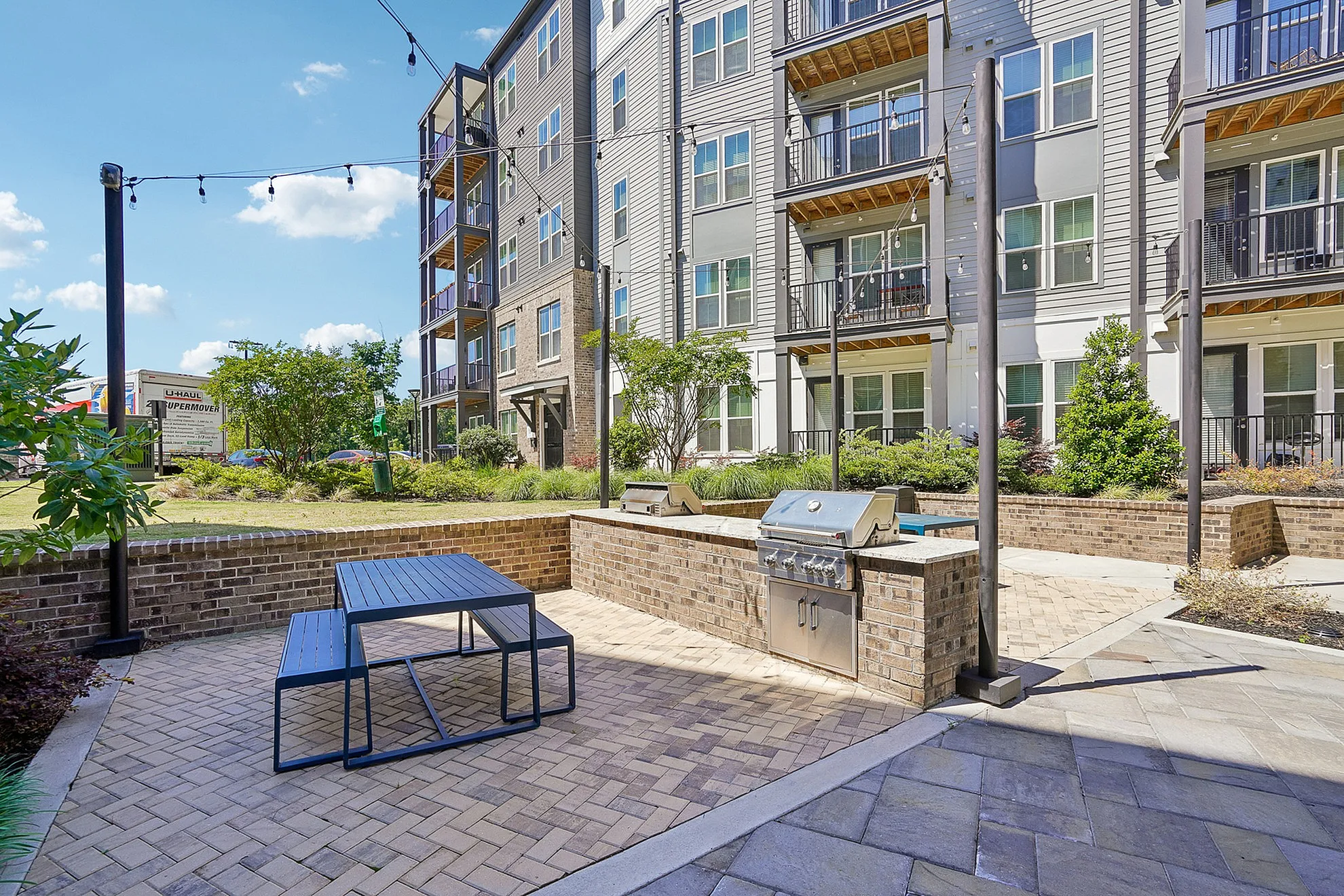 Charming apartment building with a stylish outdoor patio featuring a modern grill and picnic table, surrounded by lush greenery.