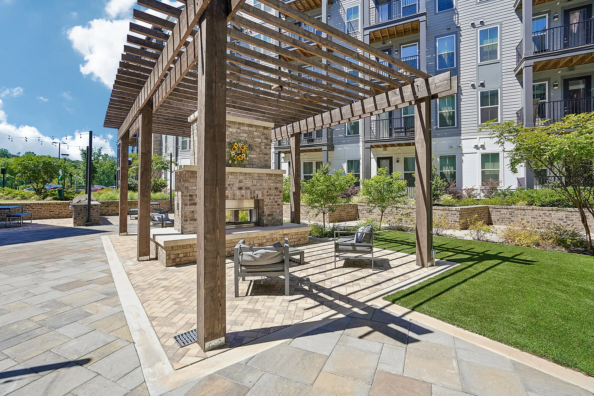 Charming outdoor seating area with modern pergola and cozy fireplace, surrounded by lush landscaping and elegant apartment façade.