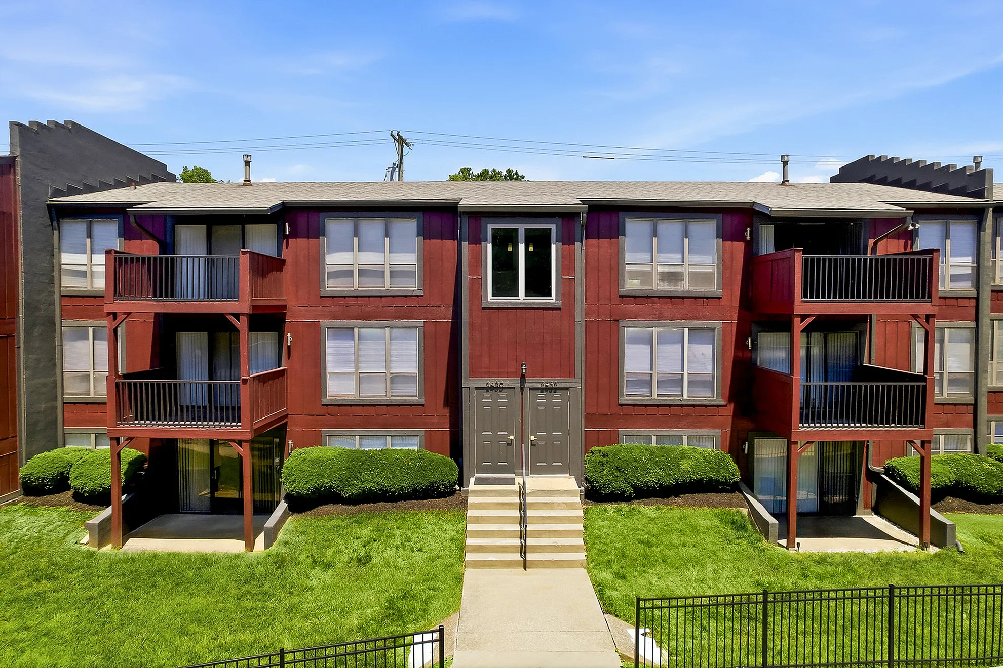 Charming red apartment building with private balconies, lush greenery, and inviting entrance in a tranquil neighborhood.