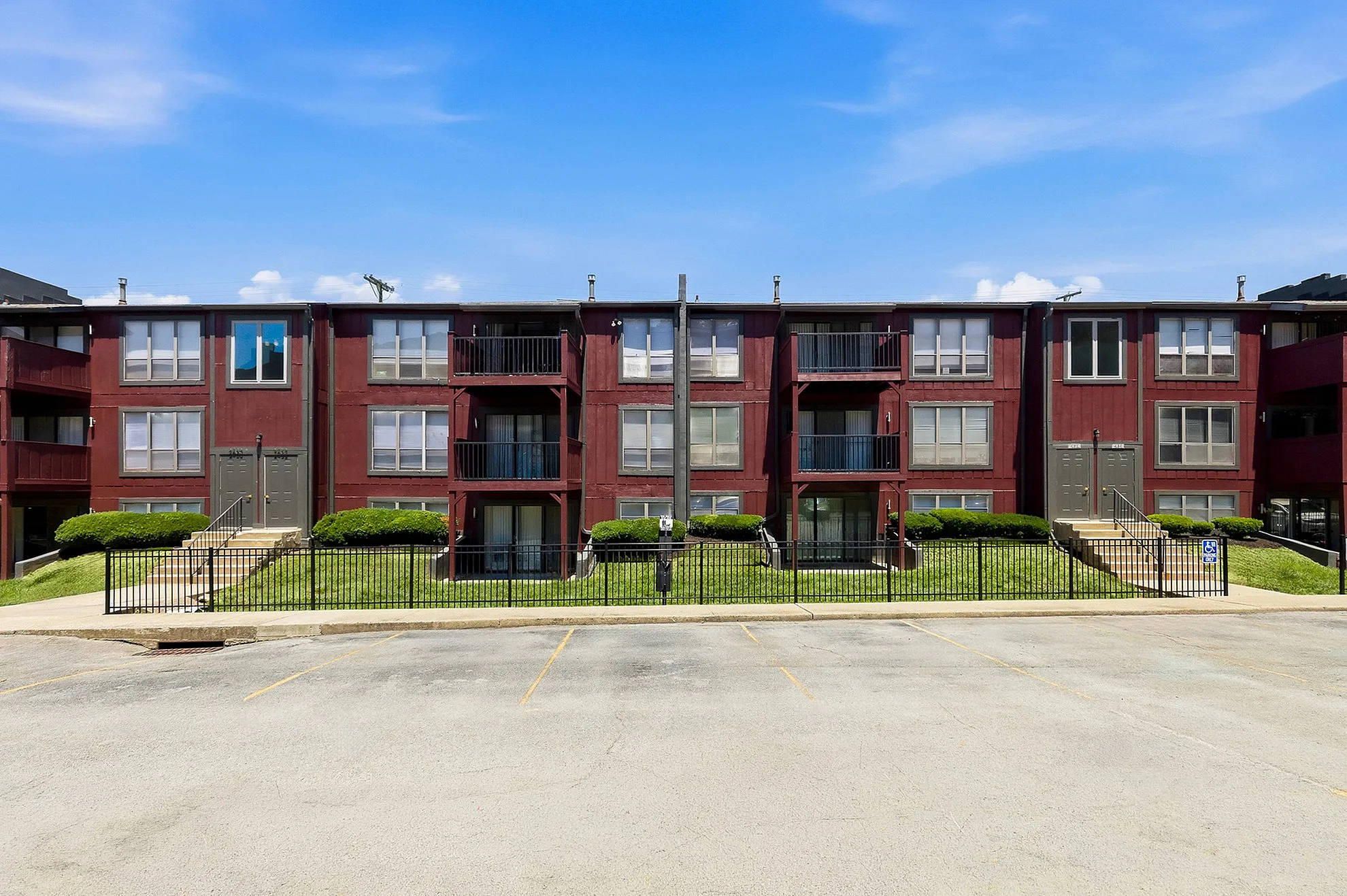 Inviting red-brick apartment building with charming balconies and lush green landscaping under a bright blue sky.