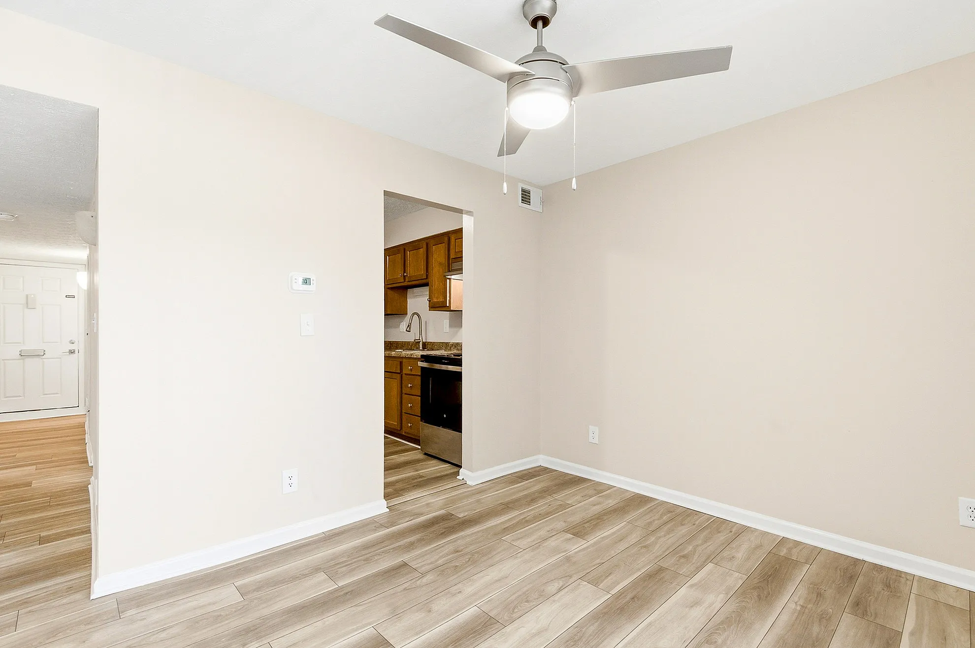 Bright apartment interior featuring sleek wooden flooring, a modern ceiling fan, and a glimpse of the stylish kitchen with granite countertops.