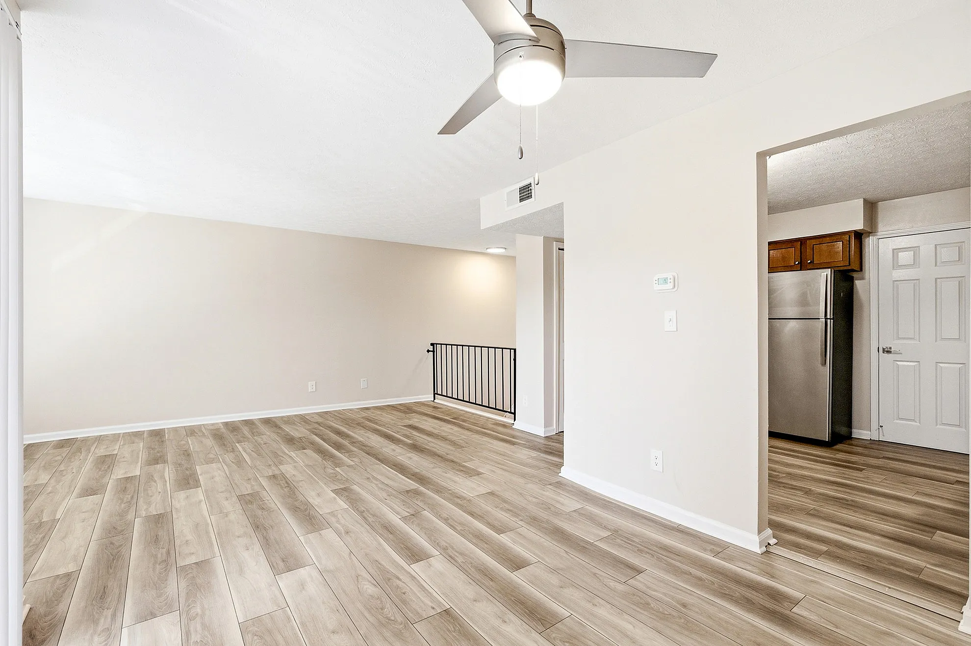 Bright and spacious living area with modern hardwood floors and ceiling fan, adjacent to a sleek stainless steel kitchen.
